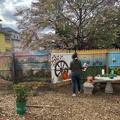 A volunteer painting a garden mural on a fence